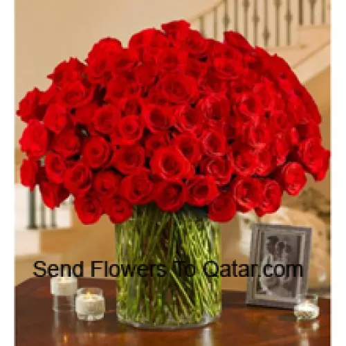 100 Roses rouges avec quelques fougères dans un grand vase en verre